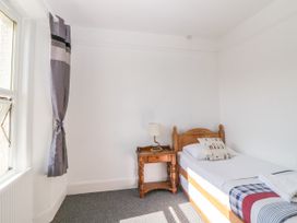 A bedroom with a single wooden bed a wooden nightstand with a lamp and a window with a curtain at 5 Stafford Road in Paignton