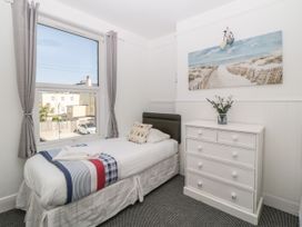 A small bedroom with a single bed beside a window and a white chest of drawers with flowers on top at 5 Stafford Road Paignton