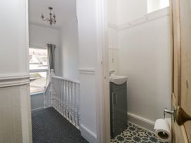 A hallway with a window and staircase railing next to a bathroom with a sink and toilet roll holder at 5 Stafford Road Paignton