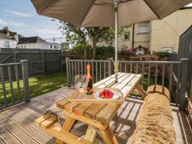 A wooden picnic table with a bottle of sparkling wine strawberries and glasses under a large umbrella on a deck in a fenced garden at 5 Stafford Road in Paignton