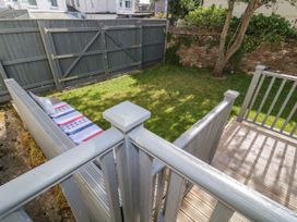 A small garden with grass a wooden deck a bench with cushions and a fence at 5 Stafford Road Paignton