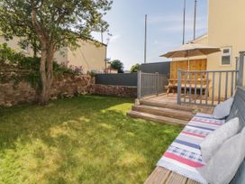 A backyard with grass a tree a wooden deck with a picnic table and umbrella and a wooden bench with cushions at 5 Stafford Road in Paignton