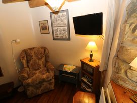A snug with an armchair, TV, lamp, and bookshelf at Penfeidr Newydd in Carningli Common, Newport, Pembrokeshire