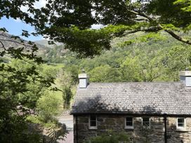 A house with a stone roof and trees in the foreground at Glyn Awel, Nant Gwynant near Beddgelert