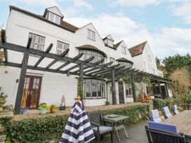 An exterior view of a white house with multiple windows and dormers a black pergola with climbing plants a patio with potted plants and wooden outdoor furniture with striped cushions and a folded striped umbrella at Riverside Manor in Evesham