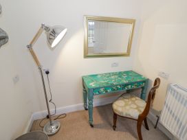 A corner with a floor lamp a decorative desk with drawers a cushioned chair and a wall mirror at Riverside Manor in Evesham