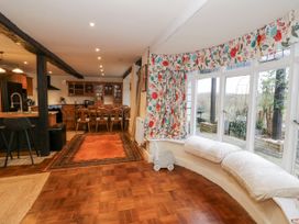 A dining area with wooden chairs and table near a kitchen and a window seating area with floral curtains at Riverside Manor in Evesham