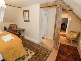 A bedroom with a wooden bed with a yellow quilt and towels a wooden beam a yellow chair with a pillow and patterned rugs at Riverside Manor in Evesham
