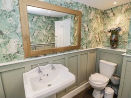 A bathroom with a white sink and toilet green paneling green wallpaper with birds and a large wooden framed mirror at Riverside Manor in Evesham