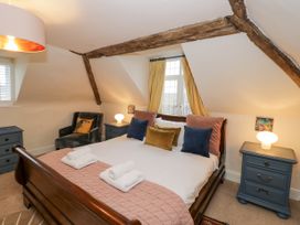 A bedroom with a wooden bed with pillows and folded towels two blue bedside tables with lamps a gray armchair and yellow curtains by a window at Riverside Manor in Evesham