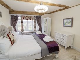 A bedroom with a bed and pillows near a window with curtains and a bench with a wardrobe and dresser on the side at Riverside Manor in Evesham