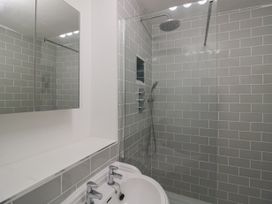 A bathroom with a white sink, dual taps, a mirrored cabinet, and a walk-in shower with grey tiled walls at Riverside Manor in Evesham