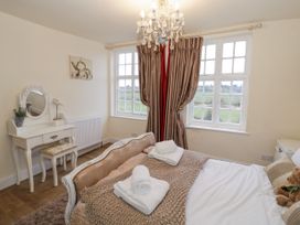 A bedroom with a bed a dressing table and windows with curtains at Riverside Manor in Evesham