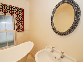 A bathroom with a white bathtub white sink a decorative round mirror and a window with patterned valance at Riverside Manor in Evesham