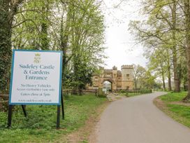 The entrance of Sudeley Castle and Gardens with a sign and driveway surrounded by trees
