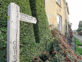 A wooden signpost for Cotswold Way public footpath next to a hedge and a stone house at Riverside Manor in Evesham