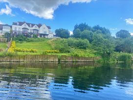 A large white house on a hill with a grassy lawn and trees by a body of water at Riverside Manor in Evesham