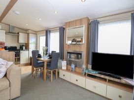 A living room with a sofa, dining table and television at Seashell Lodge, 50 Foxburrow Hang, Belton, Norfolk