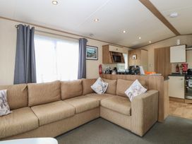A living room with a sofa and kitchen area at Seashell Lodge, 50 Foxburrow Hang, Belton, Norfolk