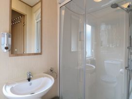 A bathroom with a sink, mirror, toilet, and shower at Seashell Lodge, 50 Foxburrow Hang, Belton, Norfolk