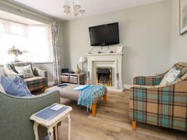 A living room with a fireplace a mounted television armchairs and a window with floral curtains at Branwen in Talacre