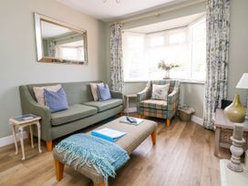 A living room with a green sofa, plaid armchair, ottoman, side tables, mirror, and window at Branwen in Talacre