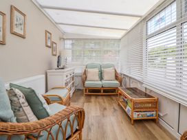 A sunroom with wicker furniture including chairs and a loveseat with cushions and a coffee table with board games at Branwen in Talacre