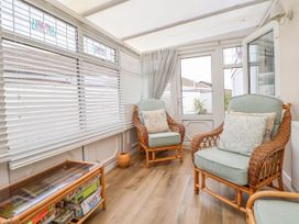 A sunroom with two wicker armchairs with cushions and a glass top wicker table with board games at Branwen in Talacre