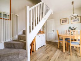 A dining area with a wooden table and chairs under a pendant light next to a carpeted staircase and a white cabinet at Branwen in Talacre