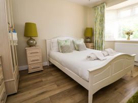 A bedroom with a white bed and wooden floor lamps on bedside tables near a window with floral curtains and wooden furniture at Branwen in Talacre