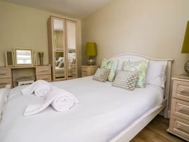 A bedroom with a white bed and rolled towels and wooden furniture including a wardrobe and bedside tables with lamps at Branwen in Talacre
