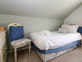 A bedroom with a single bed with white bedding and blue cushions next to a patterned chair with a blue pillow at Branwen in Talacre