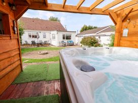 Outdoor covered hot tub on wooden deck with patio furniture and white house in the background at Branwen in Talacre