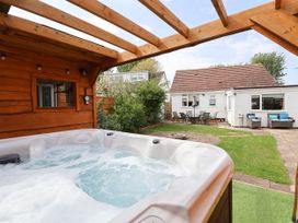 An outdoor hot tub under a wooden pergola with a garden patio and seating area at Branwen in Talacre