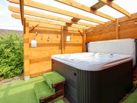 A hot tub with steps covered in artificial grass under a wooden pergola at Branwen in Talacre