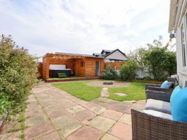 A backyard with a tiled patio and green lawn with a fire pit a wooden gazebo with a hot tub and patio furniture with blue cushions at Branwen in Talacre