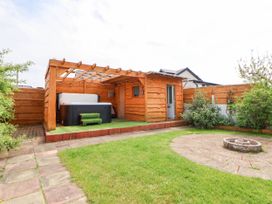 A backyard with a wooden pergola covering a hot tub and a circular stone fire pit on grass at Branwen in Talacre