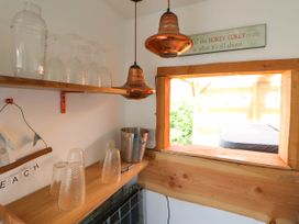 A small bar area with glassware a metal ice bucket and copper pendant lights by a wooden window at Branwen in Talacre