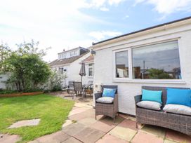 An outdoor patio area with wicker chairs and cushions next to a white house with a window and garden furniture on a paved area at Branwen in Talacre