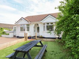 A white bungalow with a brown roof and two bay windows a wooden picnic table on grass in front and greenery to the right at Branwen in Talacre