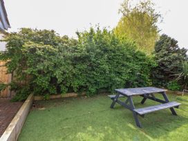 A garden with a wooden picnic table and benches on grass surrounded by dense green shrubs at Branwen in Talacre