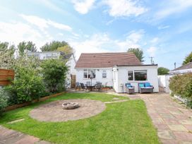 A backyard with a white house patio table and chairs and a circular stone fire pit at Branwen in Talacre