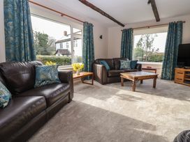 A living room with brown leather sofas blue patterned cushions and curtains wooden coffee and side tables and a television at Woodstock in Chaffcombe near Chard