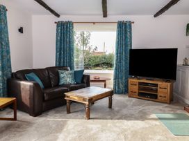 A living room with a dark sofa blue curtains a wooden coffee table and a television on a wooden stand at Woodstock in Chaffcombe near Chard