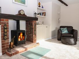 A living room with a brick fireplace and a wood burning stove a leather armchair with a cushion a floor lamp and shelves with books at Woodstock in Chaffcombe near Chard