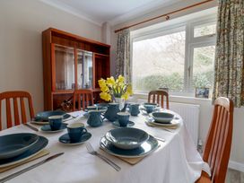 A dining room with a table set with blue dishes and cups yellow flowers in a vase wooden chairs and a glass cabinet by a window with floral curtains at Woodstock in Chaffcombe near Chard