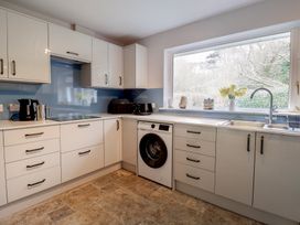 A kitchen with white cabinets a washing machine a coffee maker and a window with plants on the sill at Woodstock in Chaffcombe near Chard