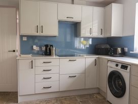 A kitchen with white cabinets blue backsplash black appliances and a washing machine at Woodstock in Chaffcombe near Chard