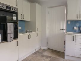 A kitchen with white cabinets a built-in oven a white door and a tiled floor at Woodstock in Chaffcombe near Chard