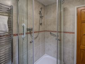 A bathroom shower area with glass doors a metal grab bar a handheld showerhead a towel rail with white towels and tiled walls at Woodstock in Chaffcombe near Chard